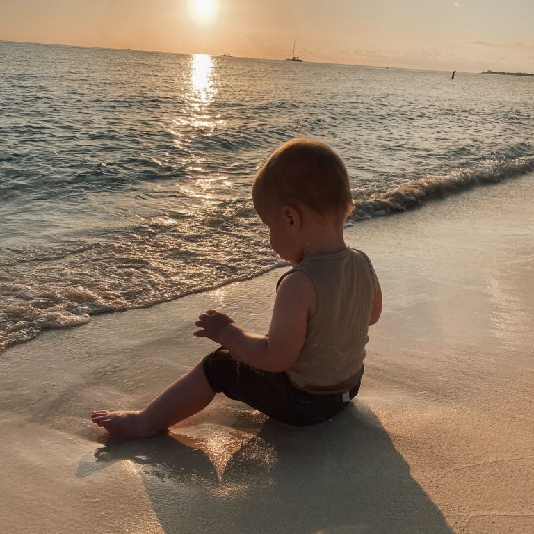 Baby sitting on beach at sunset looking at calm sea and sand in Grand Cayman