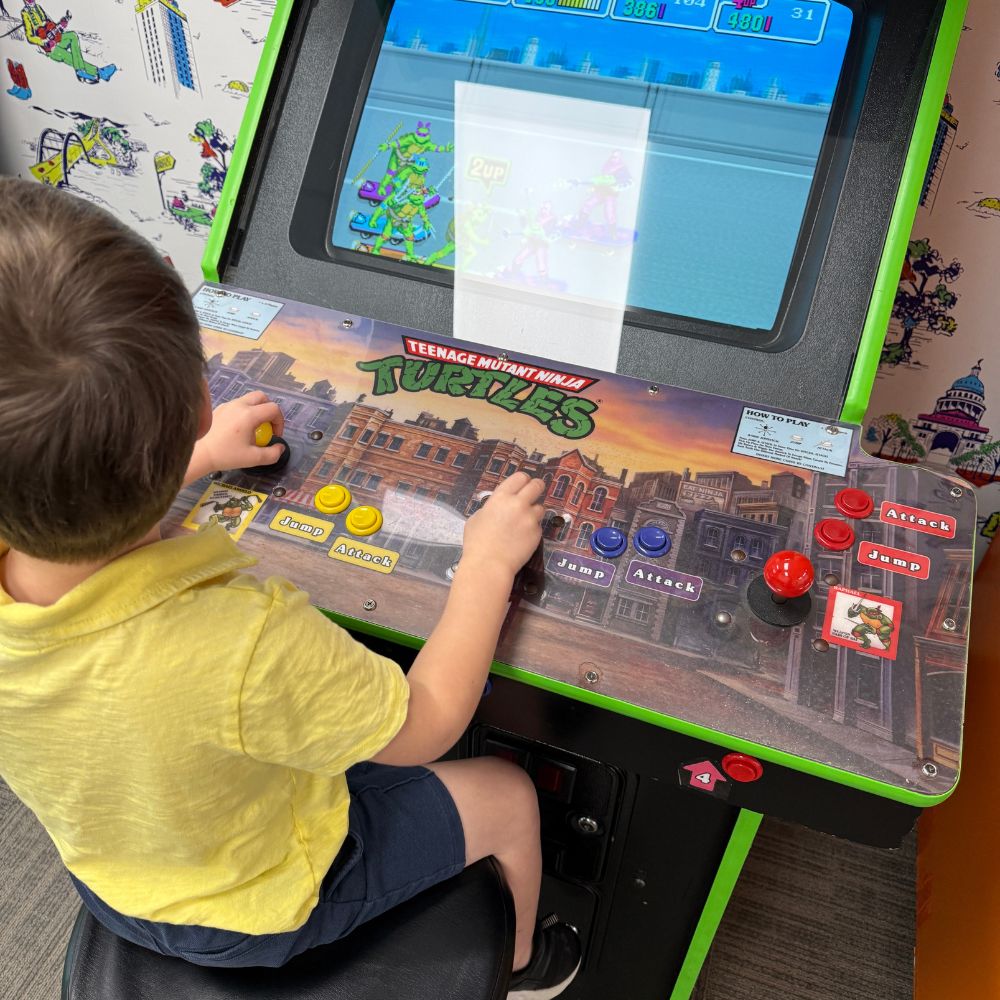 Young boy sitting at Teenage Mutant Ninja Turtle video game machine at Omni Barton Creek Resort in Austin Texas