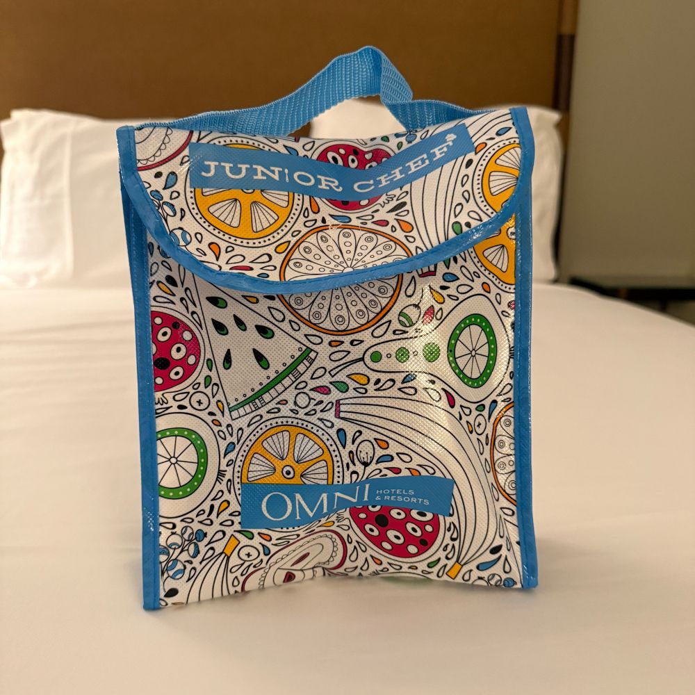 Colorful bag sitting on a bed that reads Junior Chef Omni Hotels and Resorts
