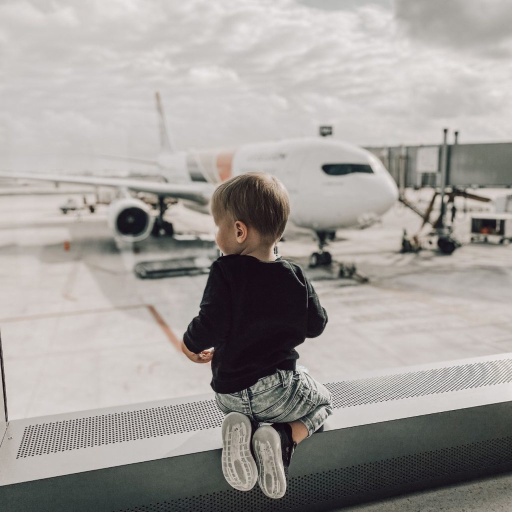 flying with a toddler looking out airport window at airplane