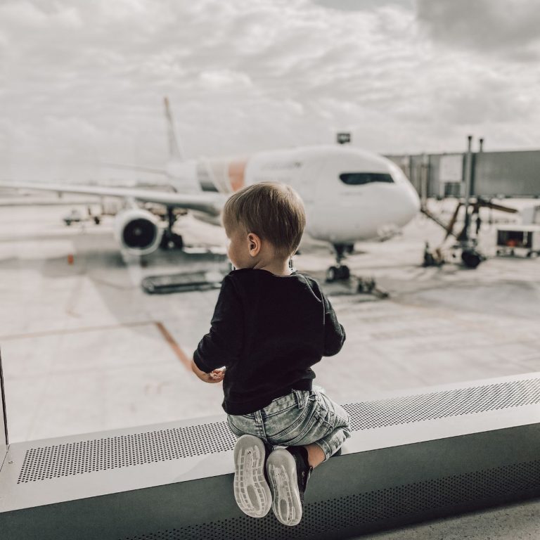flying with a toddler looking out airport window at airplane