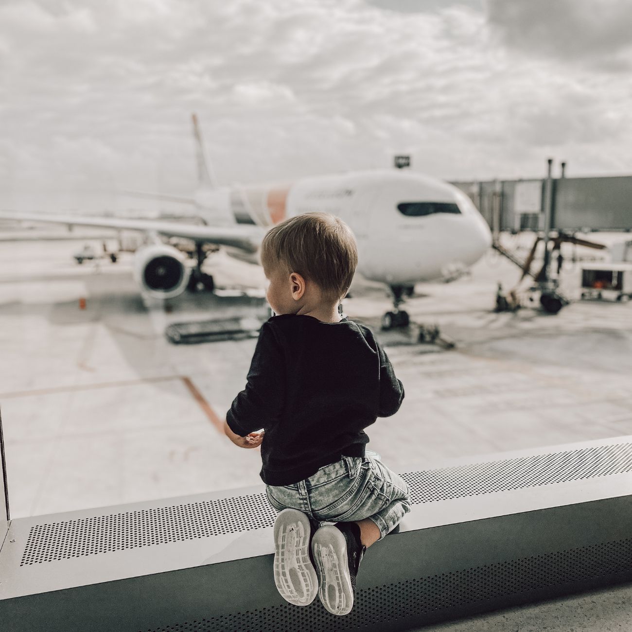 flying with a toddler looking out airport window at airplane