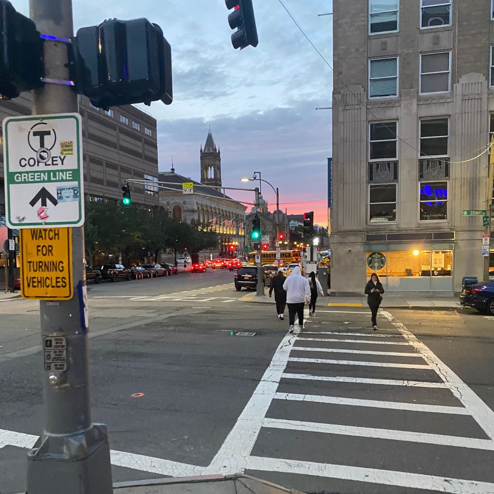 Boston street at sunset with crosswalk, stoplights and buildings in distance