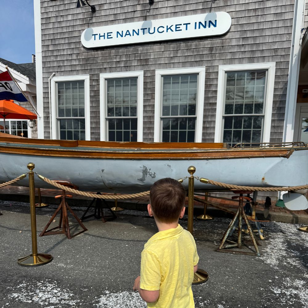Young boy standing in front of Nantucket Inn with boat in foreground